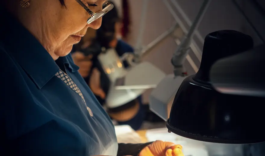 A gemmologist working at a lit bench, sorting small stones.