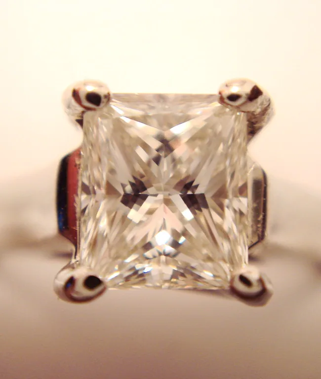 A princess-cut diamond held in four claws, photographed close up.